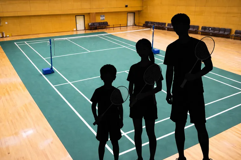 小学生・中学生・大人の身長差をシルエットで比較したバドミントンコート風景
