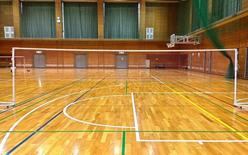 バドミントンネットをまっすぐ張った状態のコート全体と支柱位置を確認する体育館の設営完了シーン