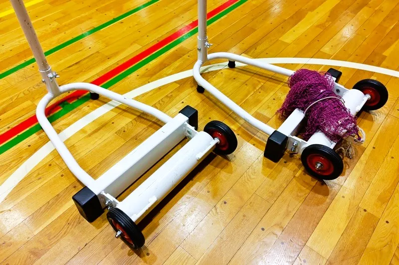 体育館に置かれたバドミントンネットと支柱｜設営前に上下とロープを確認する準備状態